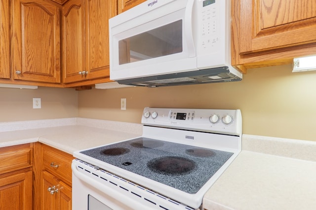 kitchen with brown cabinetry, white appliances, and light countertops