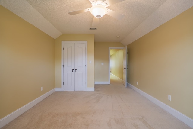 unfurnished bedroom with a textured ceiling, light colored carpet, visible vents, baseboards, and a closet