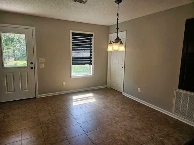 unfurnished dining area featuring dark tile patterned flooring, a healthy amount of sunlight, a textured ceiling, and an inviting chandelier