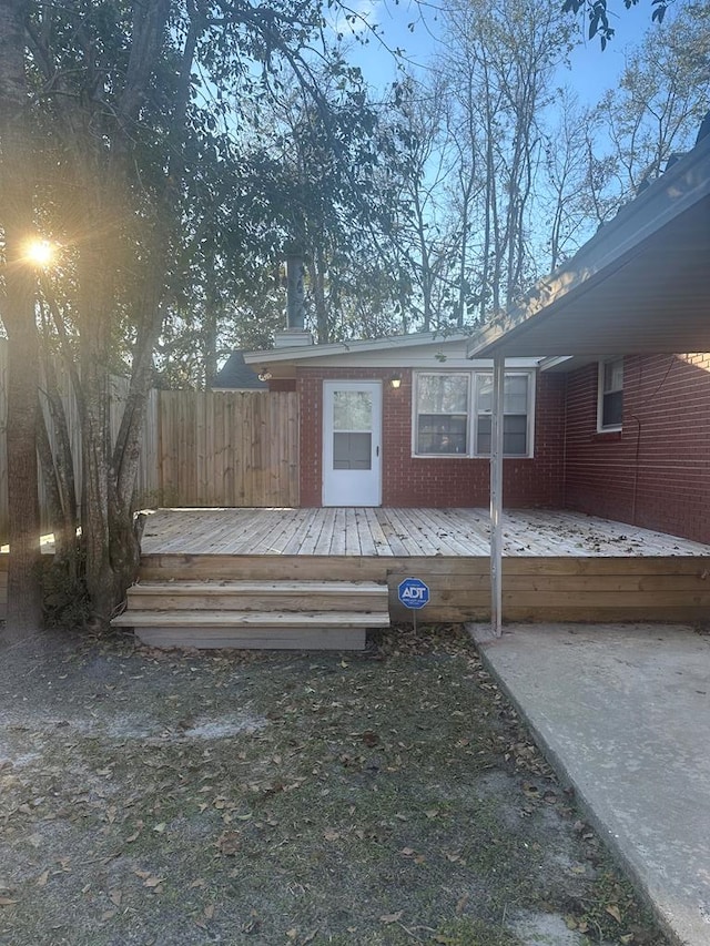 entrance to property with a deck, brick siding, and fence