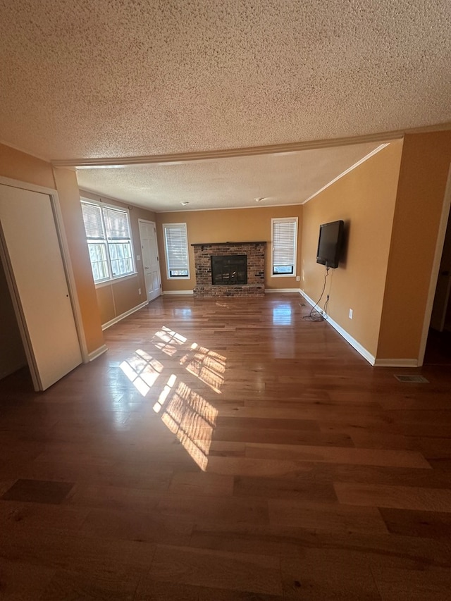 unfurnished living room featuring a textured ceiling, a fireplace, wood finished floors, baseboards, and ornamental molding