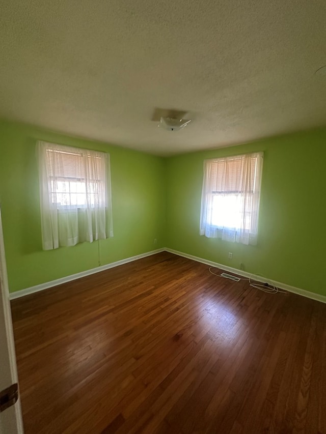 empty room featuring a healthy amount of sunlight, dark wood finished floors, a textured ceiling, and baseboards