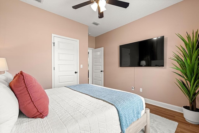 bedroom featuring a ceiling fan, visible vents, wood finished floors, and baseboards