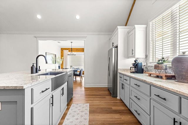 kitchen with a sink, wood finished floors, an island with sink, backsplash, and appliances with stainless steel finishes
