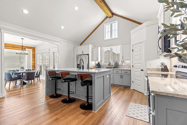 kitchen with stainless steel appliances, gray cabinets, beam ceiling, a center island with sink, and an inviting chandelier