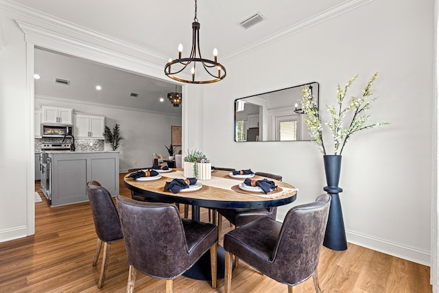 dining space with ornamental molding, a notable chandelier, visible vents, and light wood-style floors
