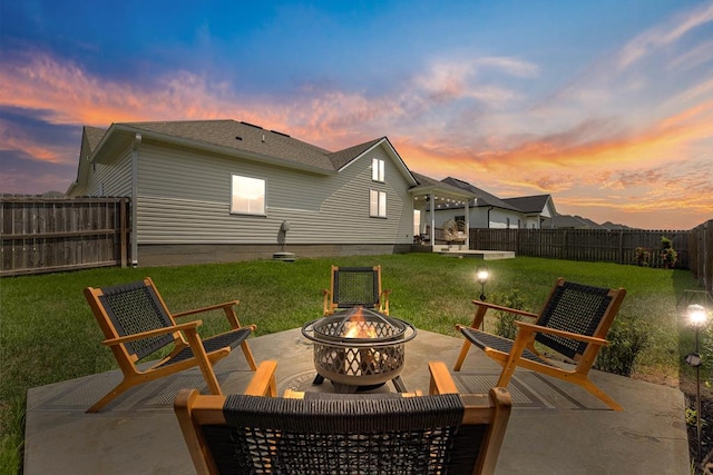 patio terrace at dusk with an outdoor fire pit, a fenced backyard, and a lawn