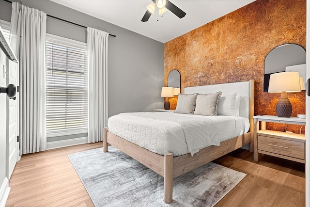 bedroom featuring baseboards, wood finished floors, a ceiling fan, and an accent wall