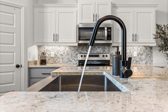 kitchen with white cabinetry, appliances with stainless steel finishes, light stone countertops, and backsplash