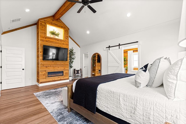 bedroom with a barn door, ornamental molding, visible vents, light wood-style floors, and vaulted ceiling with beams