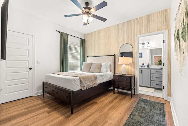 bedroom featuring light wood finished floors, wallpapered walls, connected bathroom, and baseboards