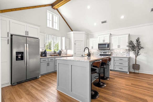 kitchen with a breakfast bar, visible vents, beamed ceiling, appliances with stainless steel finishes, and tasteful backsplash