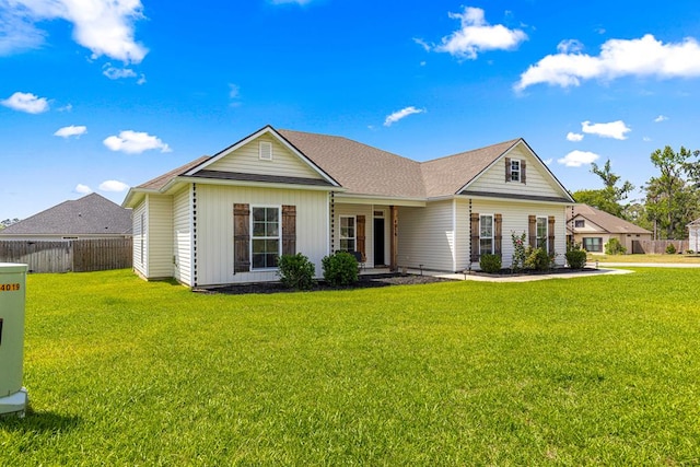 view of front facade with a front yard, a shingled roof, and fence