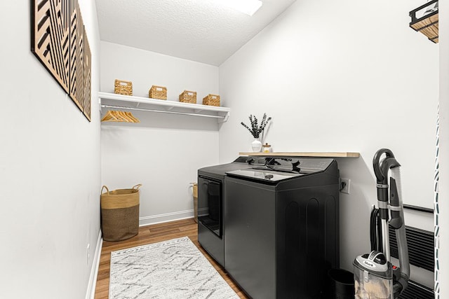 clothes washing area featuring independent washer and dryer, a textured ceiling, baseboards, wood finished floors, and laundry area