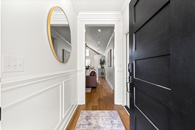 corridor with lofted ceiling, ornamental molding, a decorative wall, and wood finished floors