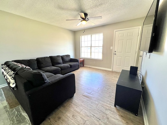 living room with ceiling fan, a textured ceiling, baseboards, and wood finished floors