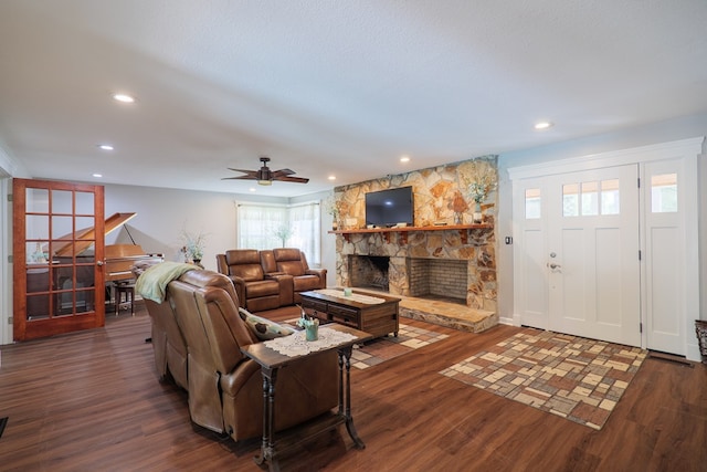 living room with ceiling fan, a stone fireplace, and dark hardwood / wood-style flooring