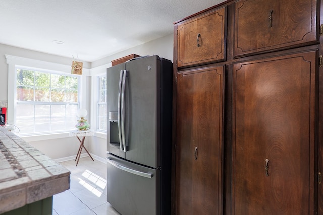 kitchen with stainless steel fridge, light tile patterned floors, and tile counters