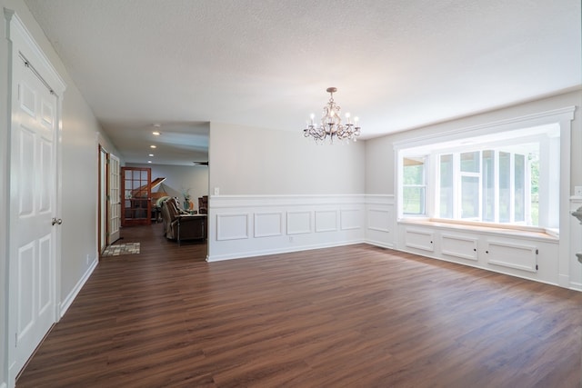 empty room with a notable chandelier, dark hardwood / wood-style floors, and a textured ceiling