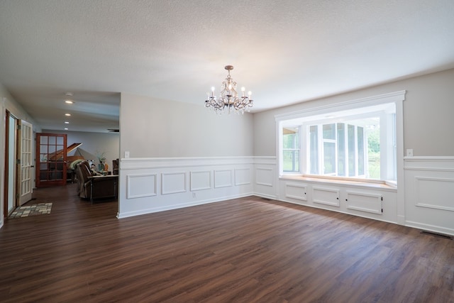 empty room with a notable chandelier, dark hardwood / wood-style flooring, and a textured ceiling