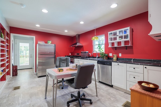 kitchen with appliances with stainless steel finishes, light wood-type flooring, wall chimney exhaust hood, decorative light fixtures, and white cabinets