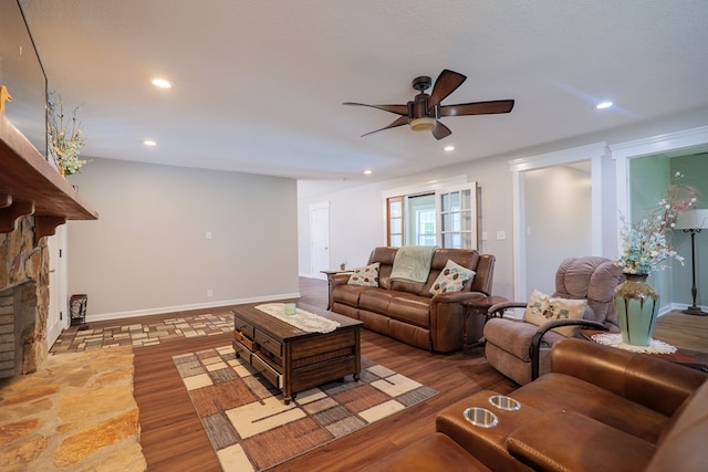 living room featuring ceiling fan, light hardwood / wood-style floors, a stone fireplace, and a textured ceiling