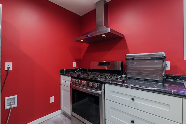 kitchen with wall chimney range hood, stainless steel range with gas cooktop, dark stone counters, light hardwood / wood-style floors, and white cabinets