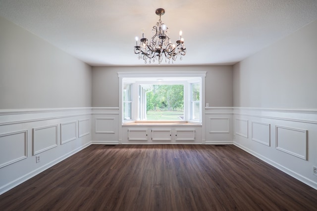 empty room with dark hardwood / wood-style floors, a textured ceiling, and an inviting chandelier