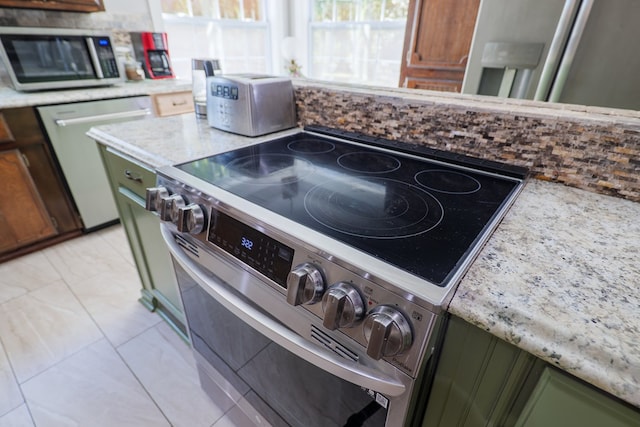 kitchen with light stone countertops, stainless steel appliances, and green cabinetry