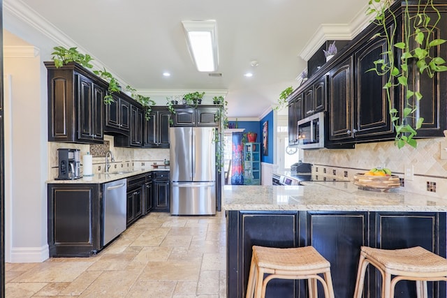 kitchen with stone tile floors, light stone countertops, a peninsula, ornamental molding, and appliances with stainless steel finishes