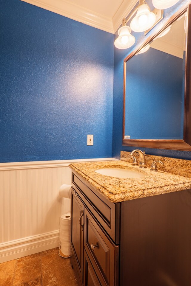 bathroom featuring vanity, ornamental molding, a textured wall, and wainscoting