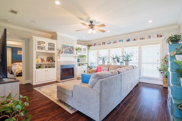 living area with visible vents, ornamental molding, a ceiling fan, dark wood-style flooring, and a tile fireplace