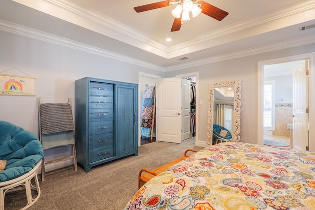 bedroom featuring a tray ceiling, ensuite bath, a walk in closet, crown molding, and light colored carpet