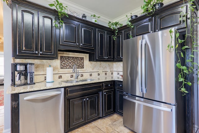 kitchen with stone tile floors, light stone counters, ornamental molding, a sink, and appliances with stainless steel finishes