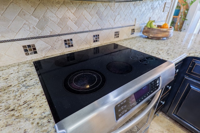 details featuring blue cabinets, decorative backsplash, light stone counters, and stainless steel range with electric cooktop