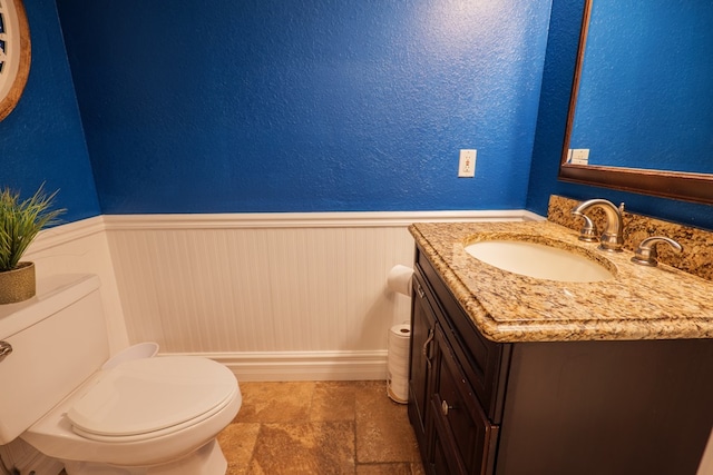 bathroom featuring vanity, toilet, wainscoting, and a textured wall