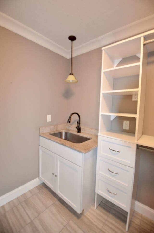 kitchen with pendant lighting, white cabinetry, crown molding, and sink