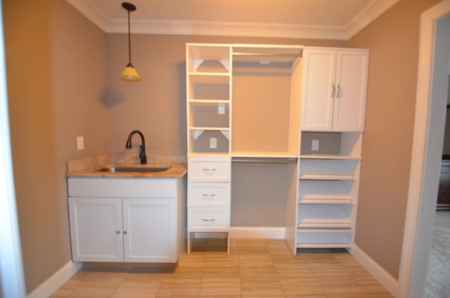 interior space featuring white cabinetry, sink, crown molding, and decorative light fixtures