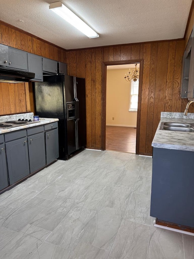 kitchen with gray cabinets, a sink, light countertops, wood walls, and under cabinet range hood