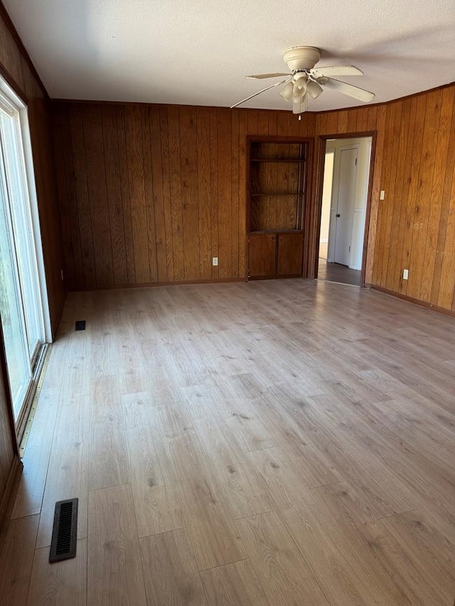 empty room featuring wooden walls, visible vents, and light wood finished floors