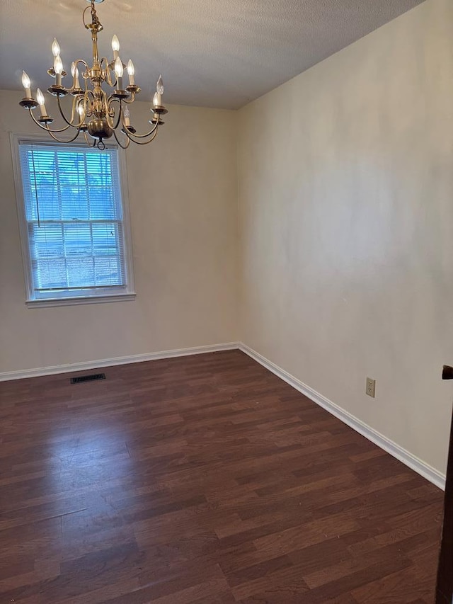 unfurnished room with dark wood finished floors, visible vents, a notable chandelier, and baseboards