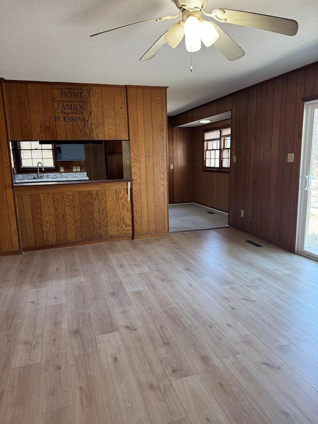 unfurnished living room with visible vents, light wood-type flooring, a ceiling fan, and a sink