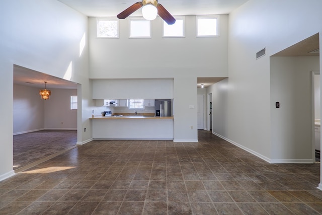 unfurnished living room with ceiling fan with notable chandelier, a healthy amount of sunlight, and a high ceiling