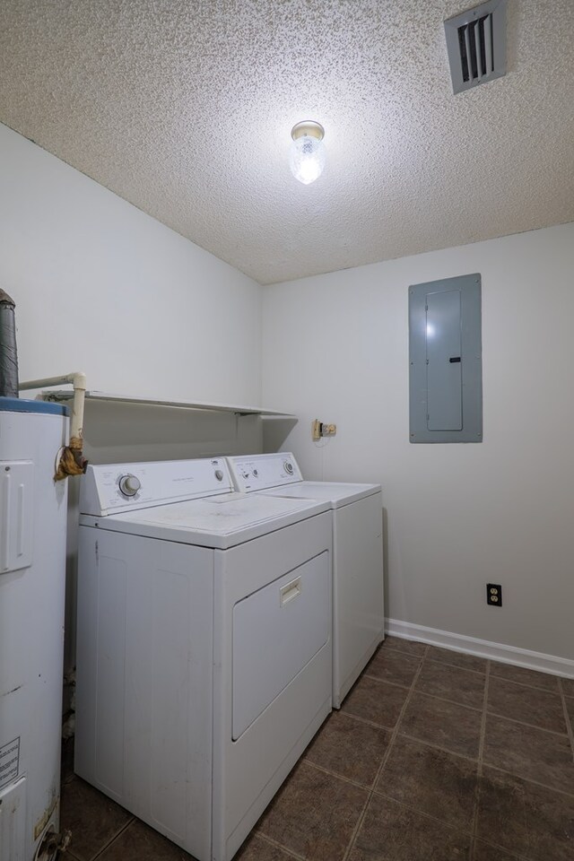 washroom with water heater, electric panel, a textured ceiling, washer and dryer, and dark tile patterned flooring