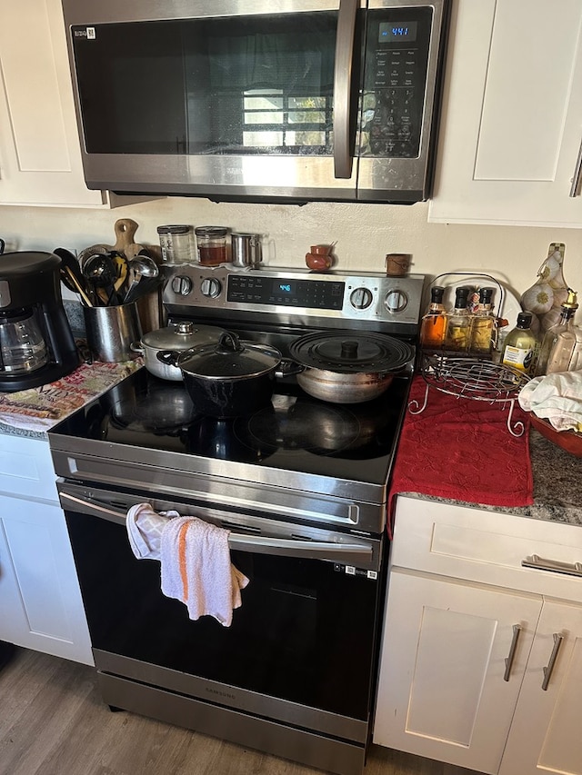 kitchen featuring wood finished floors, appliances with stainless steel finishes, and white cabinets