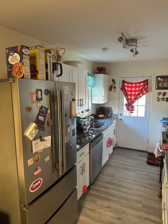 kitchen with light wood finished floors, appliances with stainless steel finishes, white cabinetry, and a sink