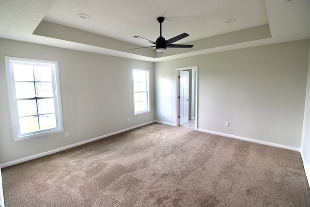 carpeted spare room with a tray ceiling, baseboards, and ceiling fan