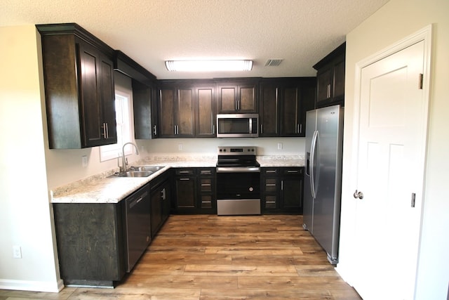kitchen featuring visible vents, a sink, light wood-style floors, a textured ceiling, and stainless steel appliances