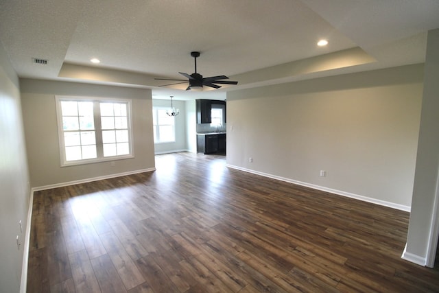 unfurnished living room with a tray ceiling, baseboards, dark wood-style floors, and visible vents