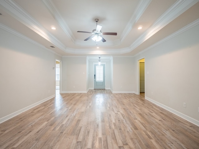 spare room featuring light wood finished floors, a tray ceiling, baseboards, and crown molding